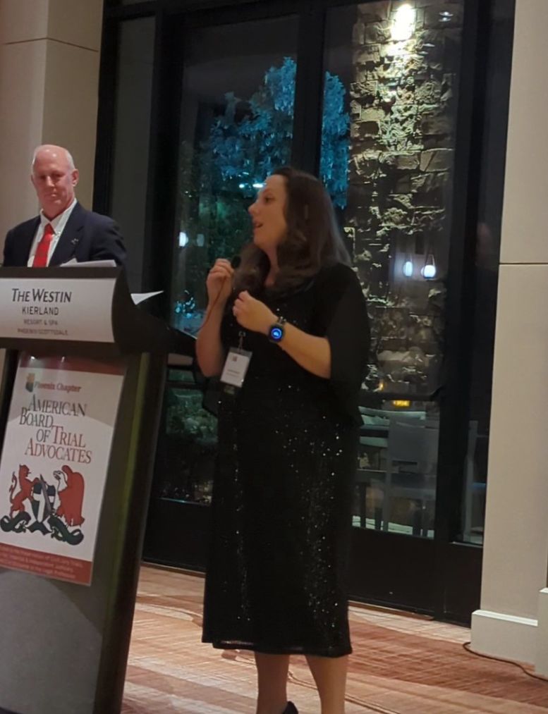 Jennifer Rebholz speaking at the ABOTA Phoenix Chapter. The American Board of Trial Advocates seal is visible at the podium.